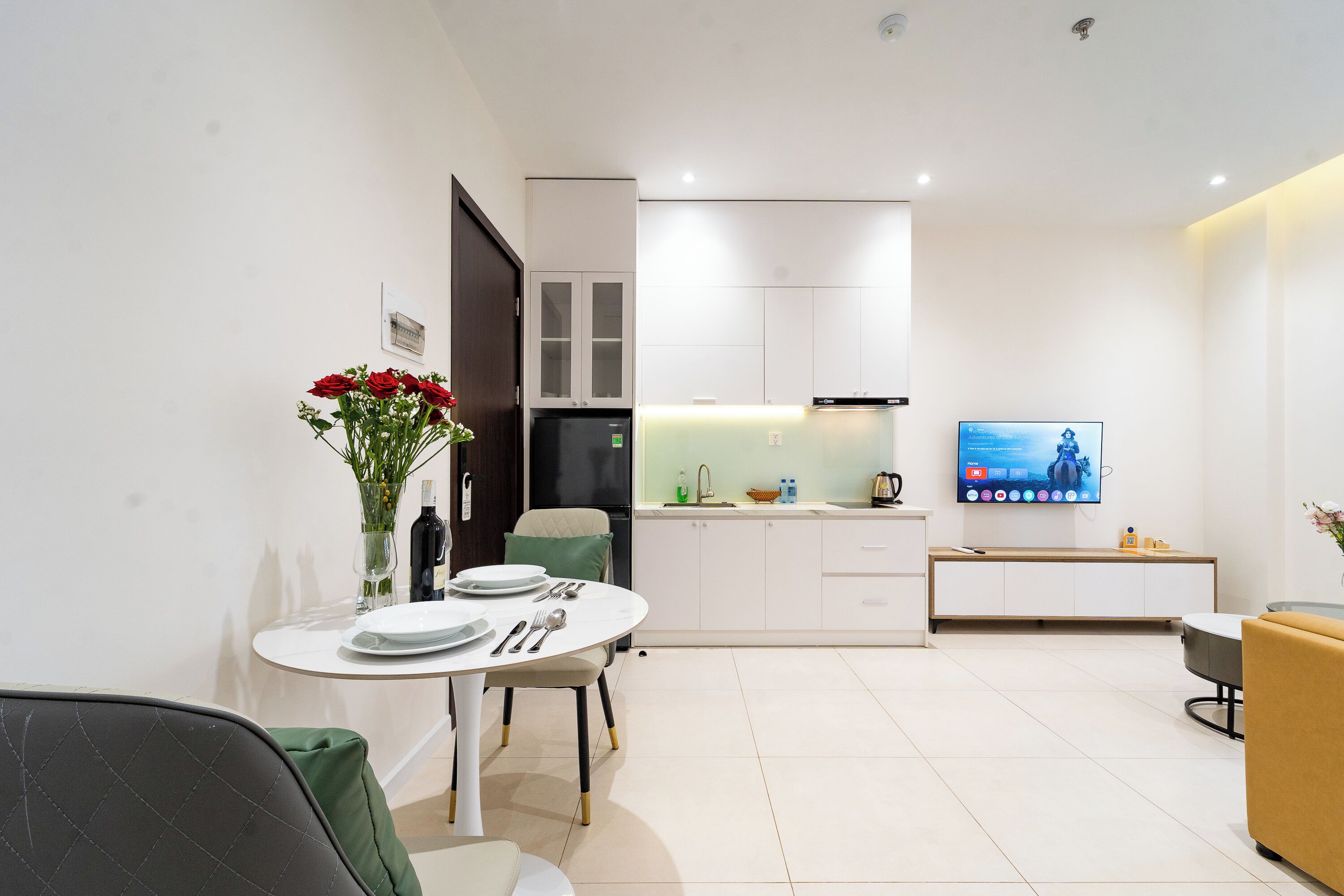 Een moderne keuken met witte kastjes, een inbouwoven en een flatscreen televisie aan de muur.