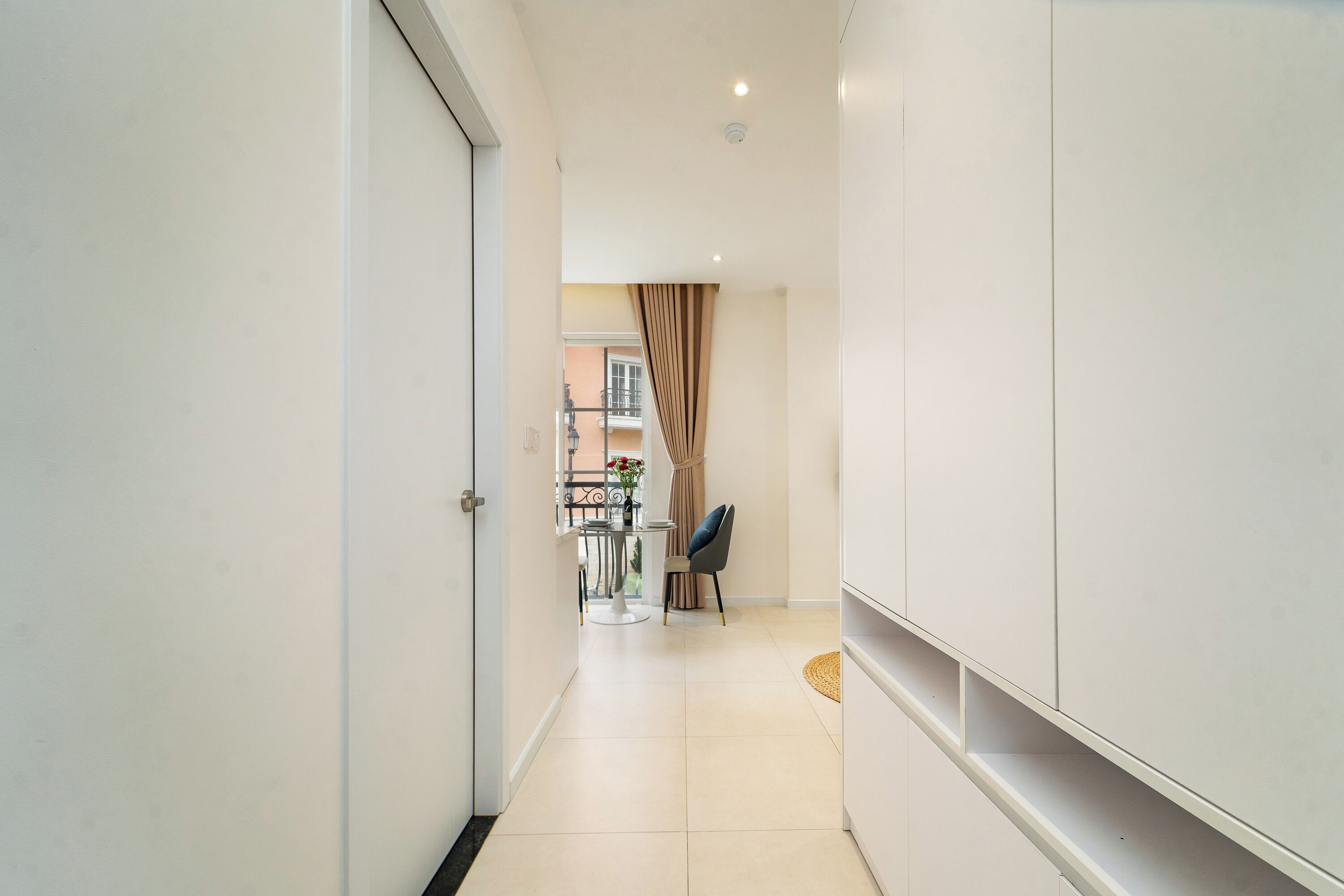 A hallway with a dining area, a chair, and a table with a vase of flowers.