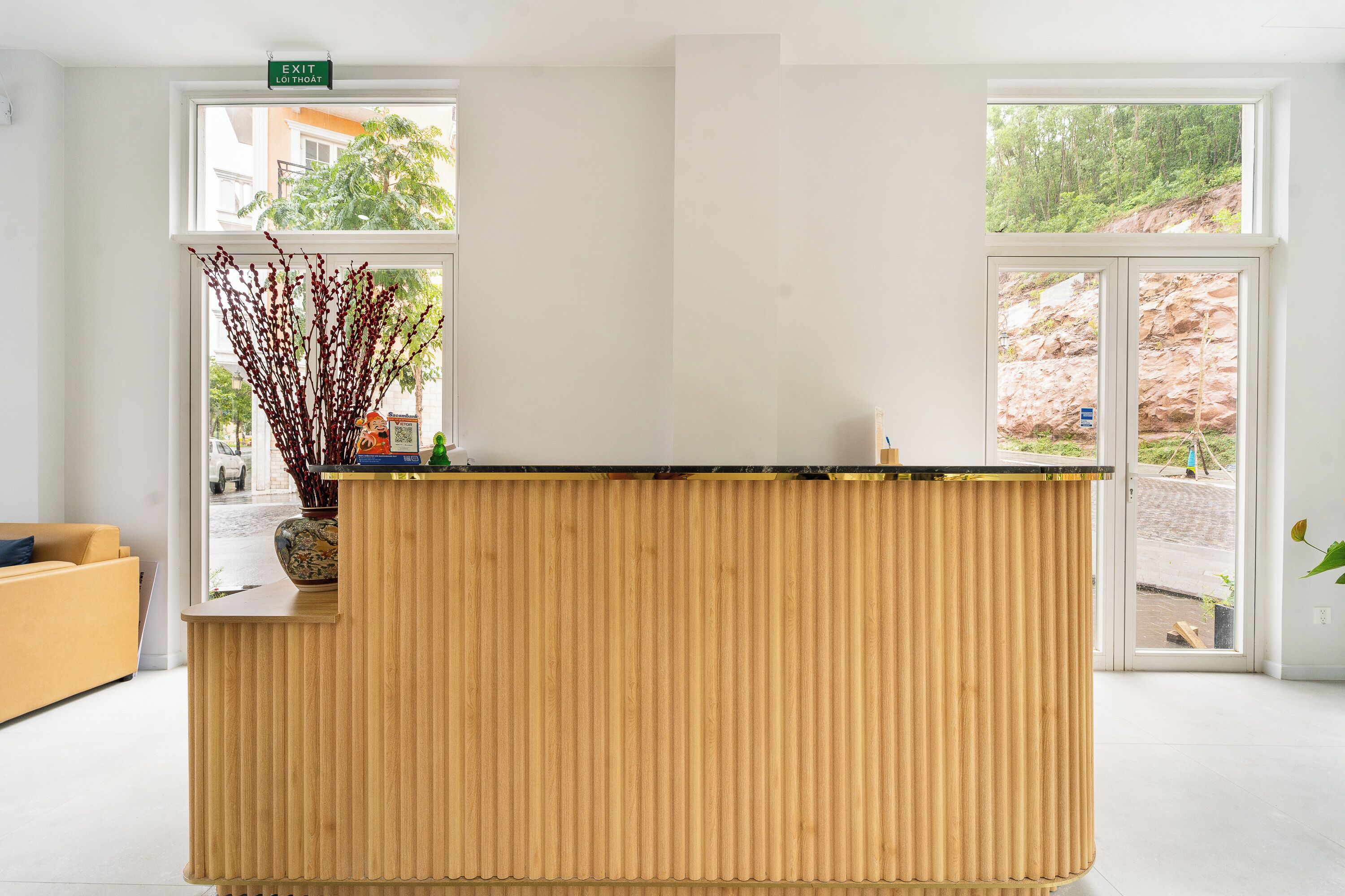 A reception desk with a wooden finish, a vase with branches, and a sign indicating an exit.
