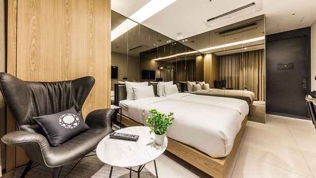 Une chambre d’hôtel moderne avec un grand lit, un fauteuil en cuir, une petite table et une plante en pot.