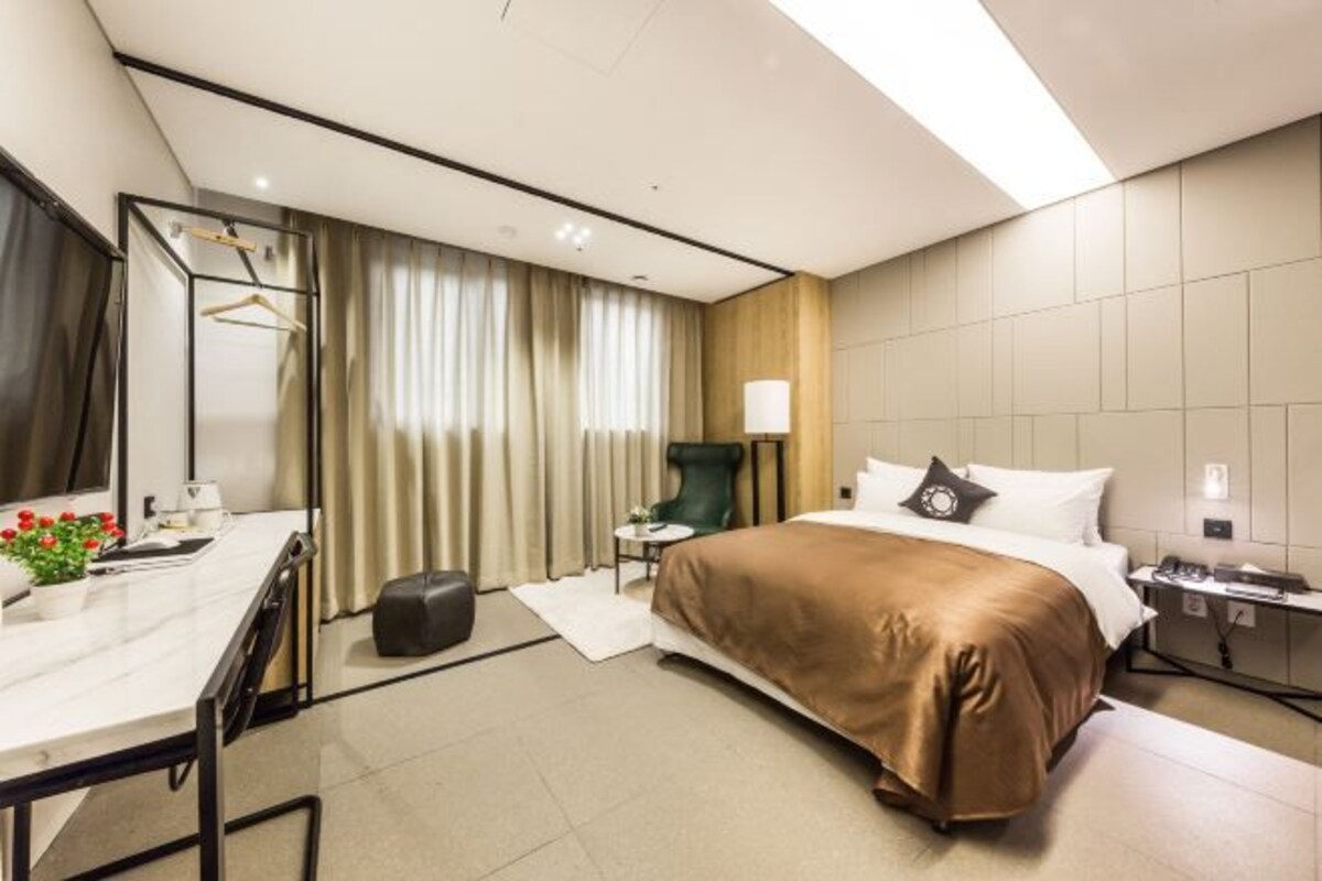 A modern hotel room with a large bed, a desk with a chair, a small table, and a chair.