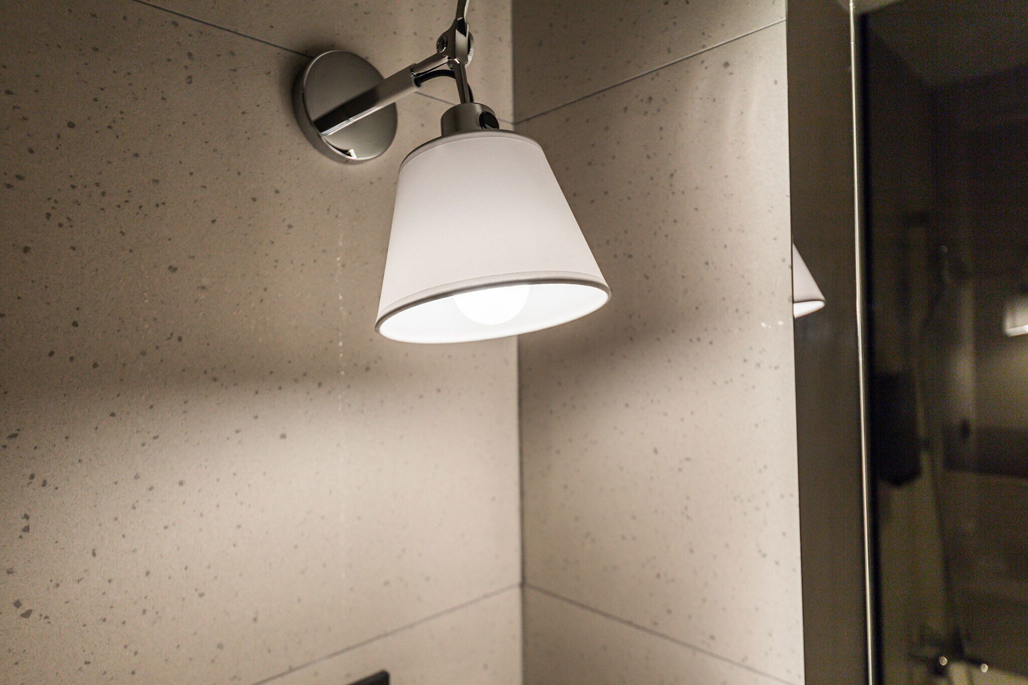 A bathroom with a white speckled tile wall, a white ceiling-mounted light fixture, and a glass shower enclosure.