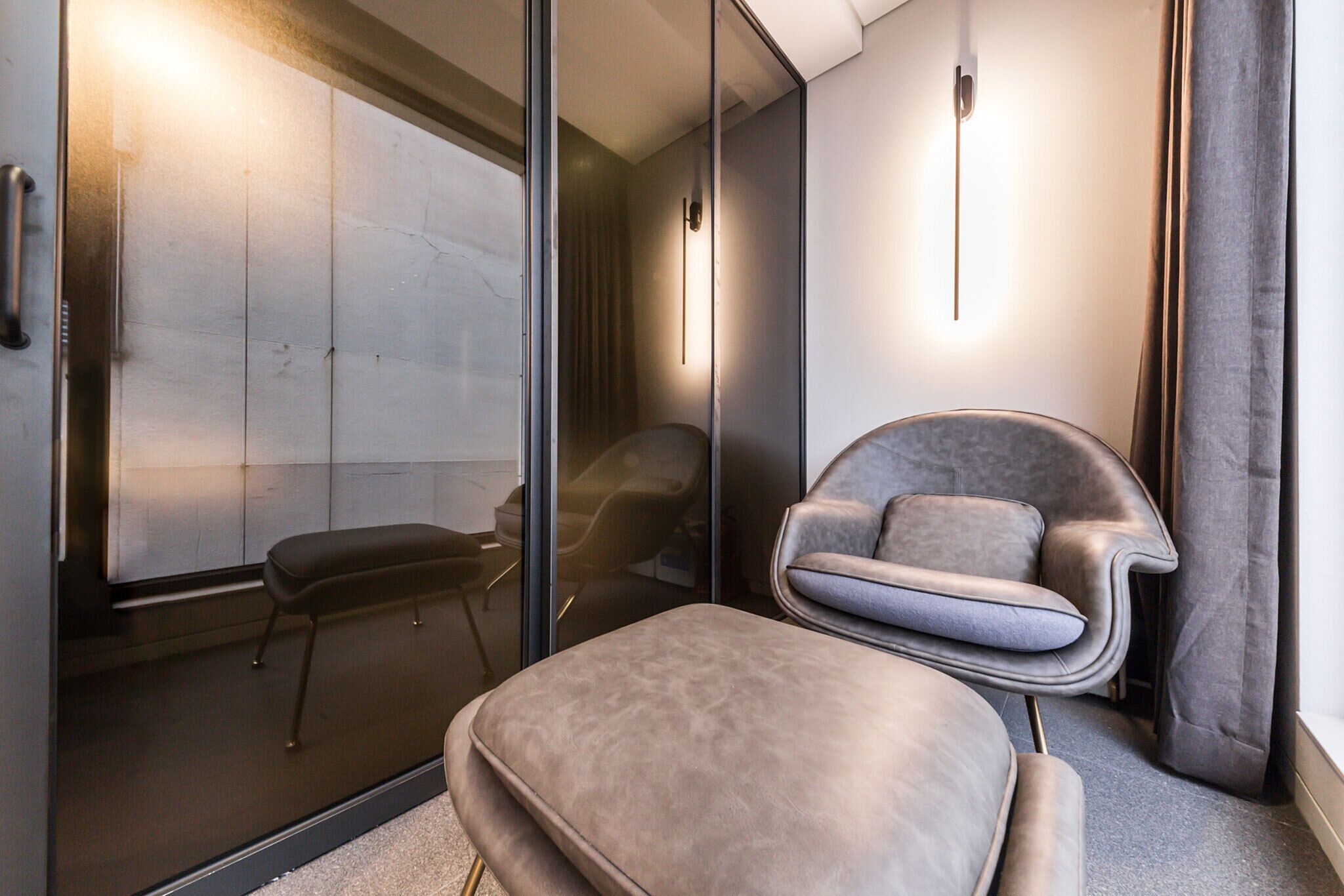 A modern interior with a glass partition, a cushioned bench, and a contemporary chair.