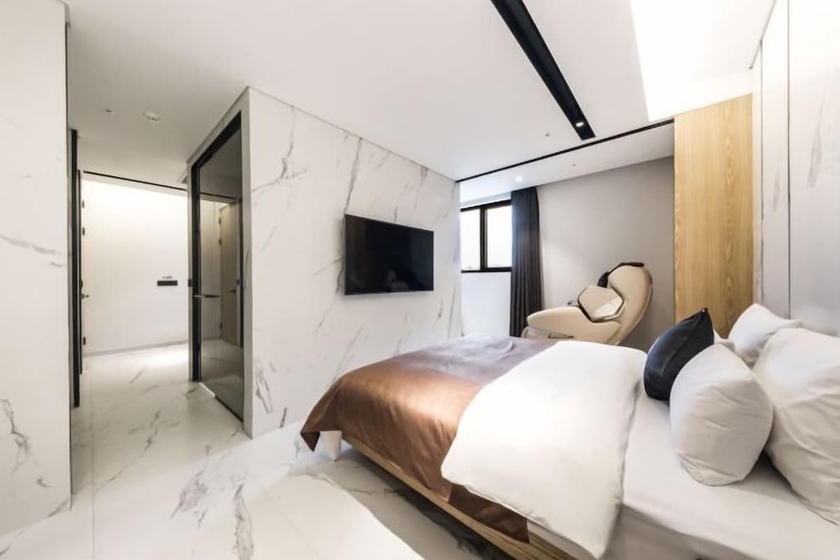 A modern bedroom with a bed, a chair, and a TV mounted on the wall.