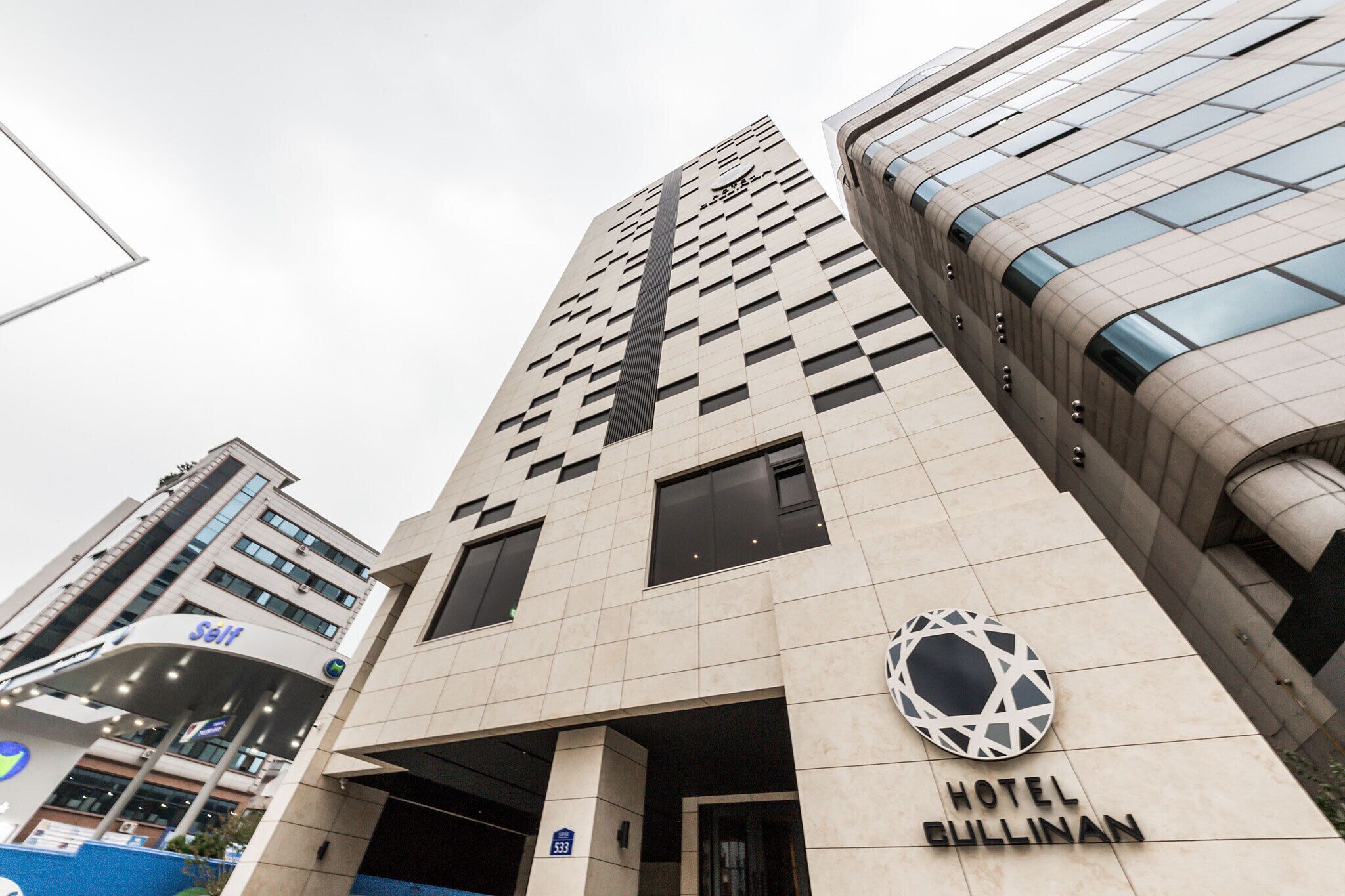 Un moderno edificio de hotel con un logotipo destacado, una entrada amplia y una vista despejada del entorno urbano.