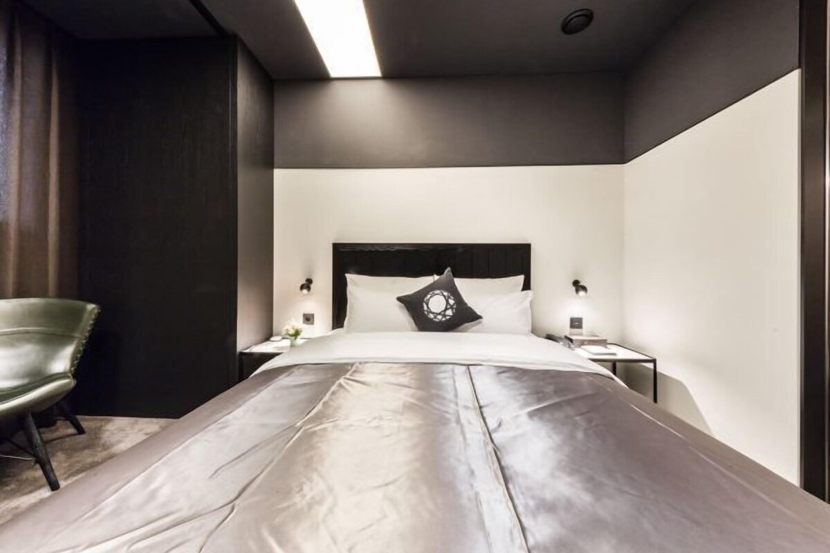 A modern hotel room with a large bed, a green chair, and a nightstand with a lamp.
