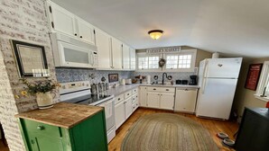A kitchen with white cabinets, a microwave, a stove, a sink, and a refrigerator. There is a green cabinet and a rug on the floor.