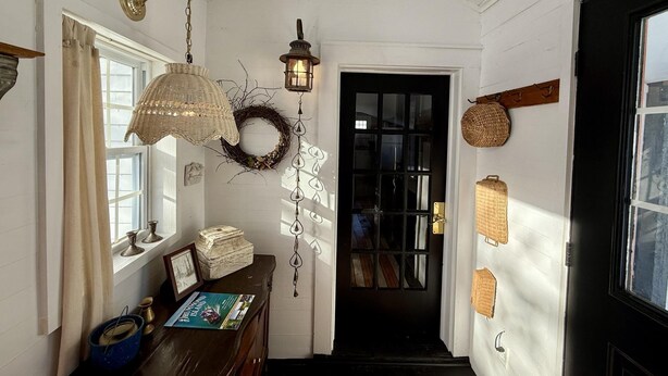 A hallway with a wooden bench, a wicker lamp, a lantern, a wreath, and wicker baskets on the wall.