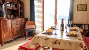A dining area with a table set for two, a wooden cabinet, and a view through a glass door. - Les Bluets by Interhome (Les Mosses)