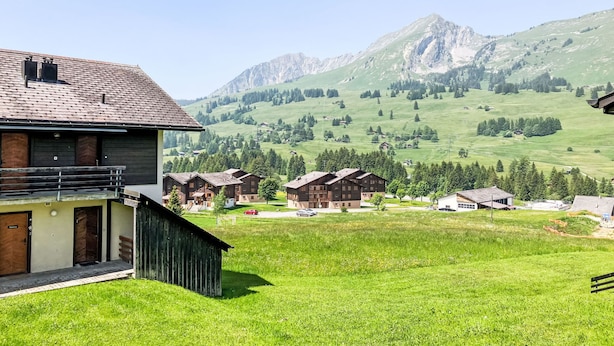 A mountain village with traditional wooden houses, a grassy courtyard, and a view of distant mountains. - Les Bluets by Interhome (Les Mosses)