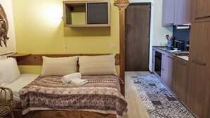 A bedroom with a bed, a bedside table, a chair, a wooden wardrobe, and a small kitchen area with a sink and countertop. - Les Bluets by Interhome (Les Mosses)
