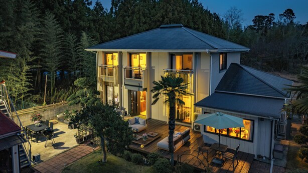 Une maison à deux étages dotée d’un balcon, d’une terrasse avec mobilier d’extérieur et offrant une vue sur la forêt environnante.