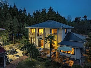 Une maison à deux étages dotée d’un balcon, d’une terrasse avec mobilier d’extérieur et offrant une vue sur la forêt environnante.