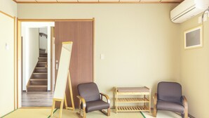 Une pièce avec un sol recouvert de tatamis, un bureau en bois, deux chaises, une petite étagère et une porte coulissante donnant sur un escalier.