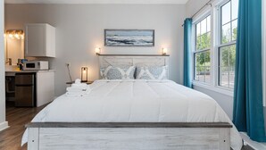 A bedroom with a bed, a bedside table with towels, a nightstand with a lamp, a window with curtains, and a view of the outdoors. - Spacious 8 Bed Suite Combo – Units 441 & 442 | Sleeps 10-12 (Old Orchard Beach)