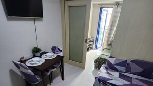 A compact living space with a dining area, a sofa, and a television mounted on the wall. - Cozy 1BR at Sea Residences Near MOA - Wifi & Netflix (Pasay)