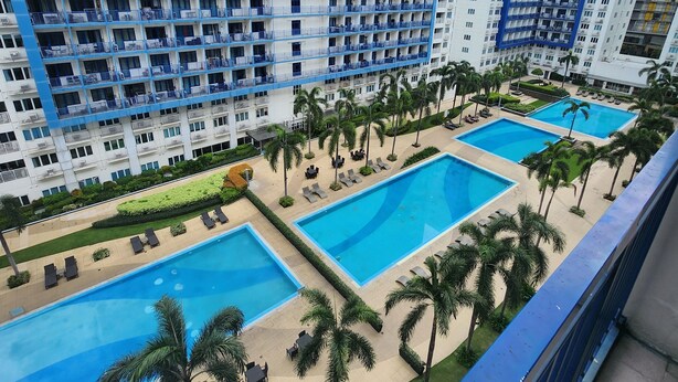 A high-rise hotel with multiple balconies and a pool area with palm trees. - Cozy 1BR at Sea Residences Near MOA - Wifi & Netflix (Pasay)
