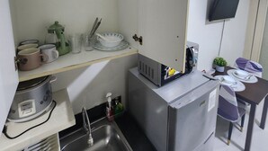 A compact kitchen with a sink, a small refrigerator, a microwave, and a TV mounted on the wall. - Cozy 1BR at Sea Residences Near MOA - Wifi & Netflix (Pasay)