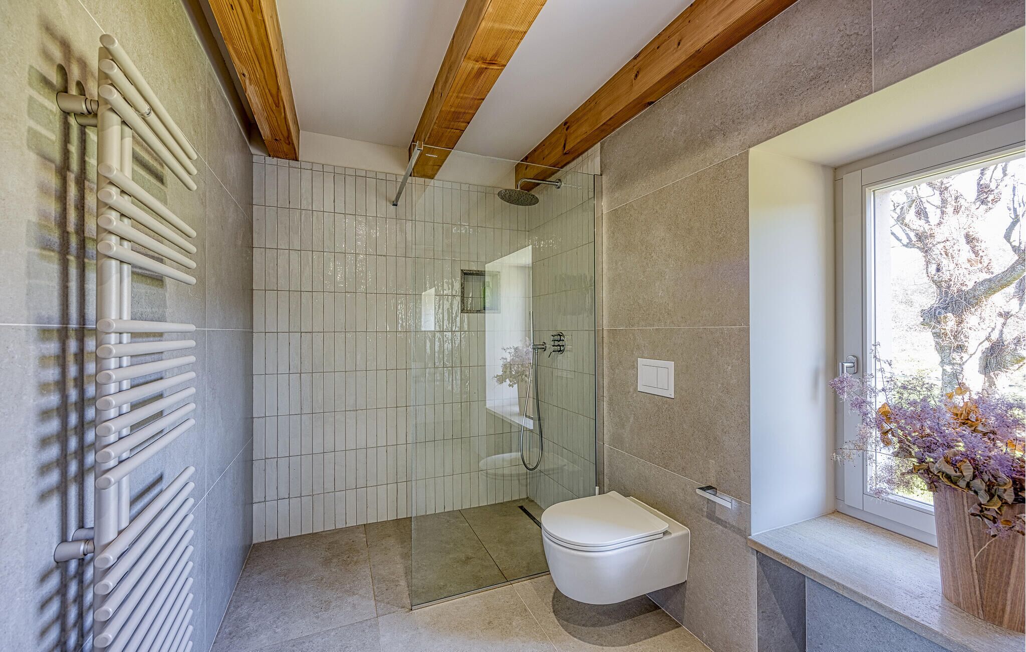 Une salle de bain moderne avec une douche à l’italienne en verre, des toilettes et une fenêtre donnant sur la verdure.
