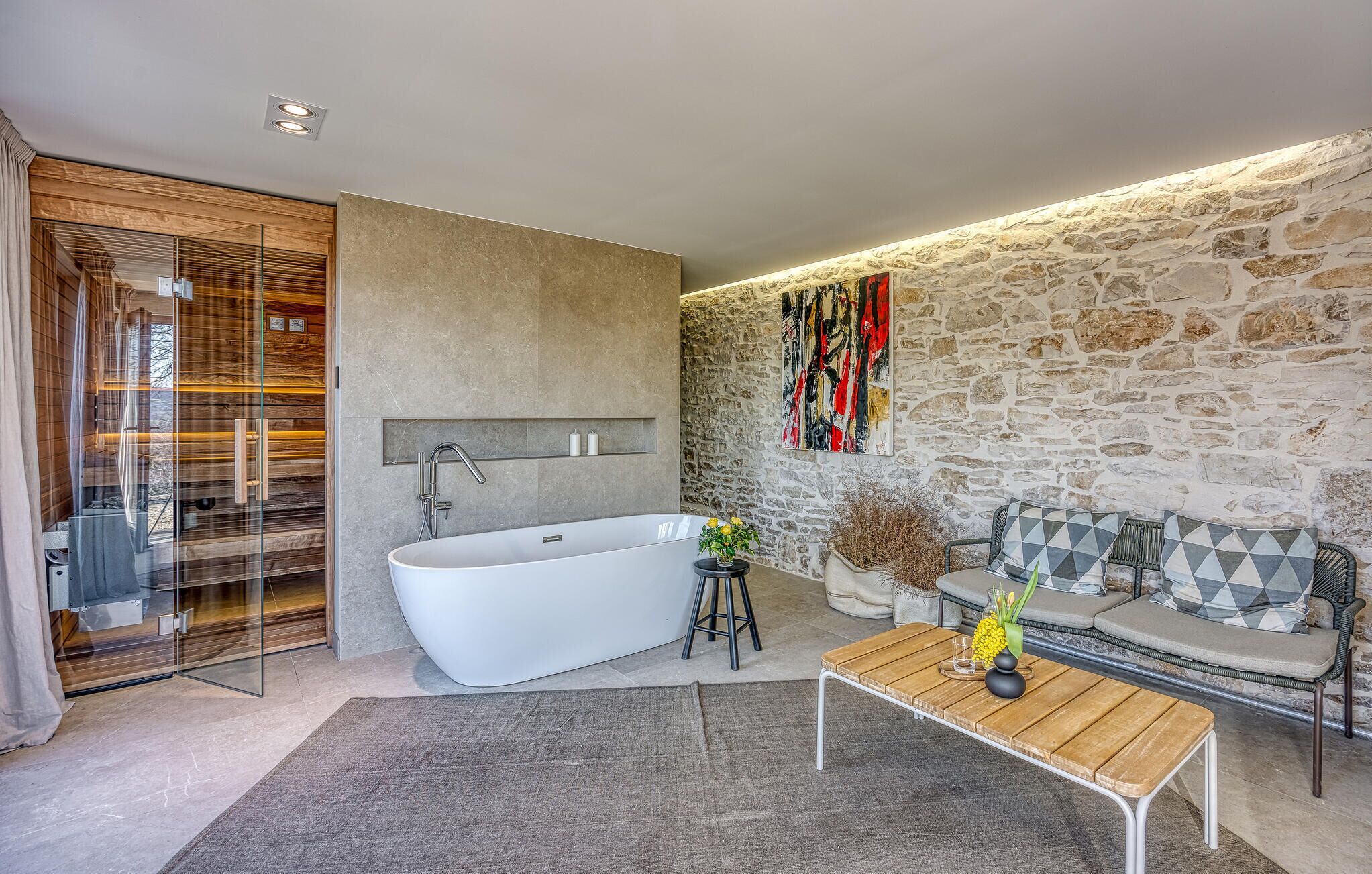 A modern bathroom with a freestanding bathtub, a glass shower enclosure, and a stone wall.