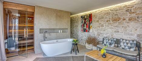 A modern bathroom with a freestanding bathtub, a glass shower enclosure, and a stone wall.