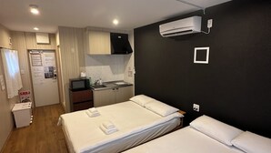 Hotellihuone, jossa on kaksi sänkyä, pieni keittiönurkkaus, pieni kylpyhuone ja kattoon asennettu ilmastointilaite.