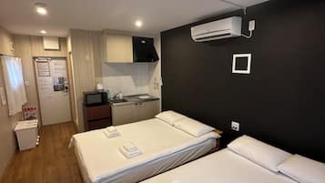 A hotel room with two beds, a kitchenette, a small bathroom, and a ceiling-mounted air conditioning unit.