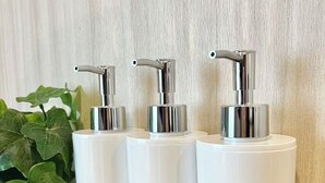 Kolme valkoista, sylinterinmuotoista annostelijaa, joiden yläosat ovat metallia, on asetettu puupinnalle kuvioidun seinän eteen.