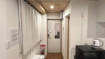 A narrow hallway with wooden flooring, a white cabinet, a black microwave, and a door with informational posters.