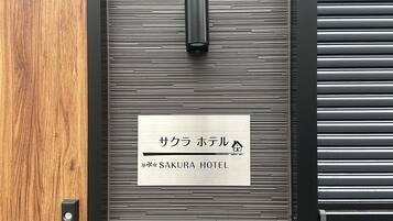 A hotel entrance with a wooden door and a metal panel wall. A sign indicates the name 'SAKURA HOTEL'.