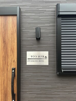 A hotel entrance with a wooden door and a metal panel wall. A sign indicates the name 'SAKURA HOTEL'.