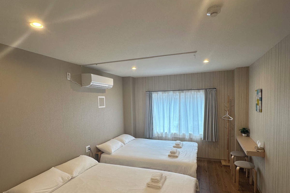 Una habitación de hotel con dos camas, un escritorio, una silla y un ventanal con cortinas.