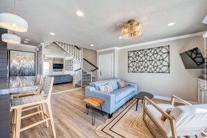 Un'ampia zona giorno con un divano blu, sedie in legno, un tavolo da pranzo e una scala che conduce a un piano superiore.