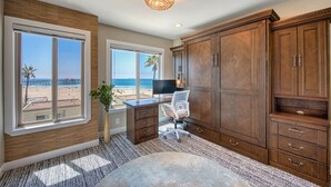 Ein Zimmer mit großen Fenstern und Meerblick, einem Schreibtisch mit Stuhl sowie Holzschränken.