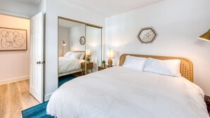 Quarto de hotel com uma cama grande, guarda-roupa, mesa de cabeceira com abajur e espelho fixado na parede.