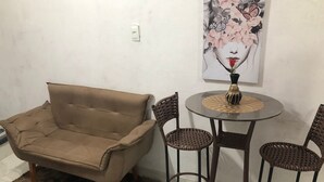 Un saló amb un sofà marró, dues cadires de vimetla, una taula rodona petita amb un ram i un quadre penjat a la paret.