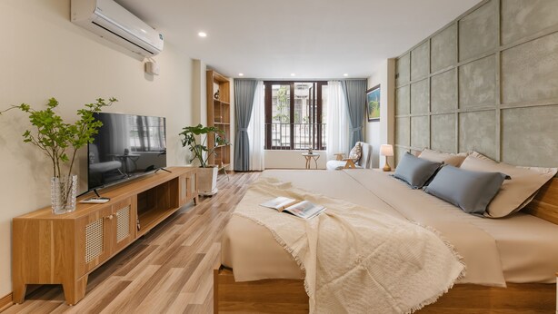 A modern hotel room with a large bed, a TV on a wooden console, a balcony with a view, and a large window with curtains.