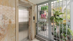 A room with a marble wall, a sliding door, and a view of a balcony with potted plants and a green umbrella.