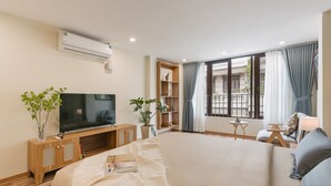A hotel room with a large bed, a TV, a bookshelf, and a balcony with curtains.