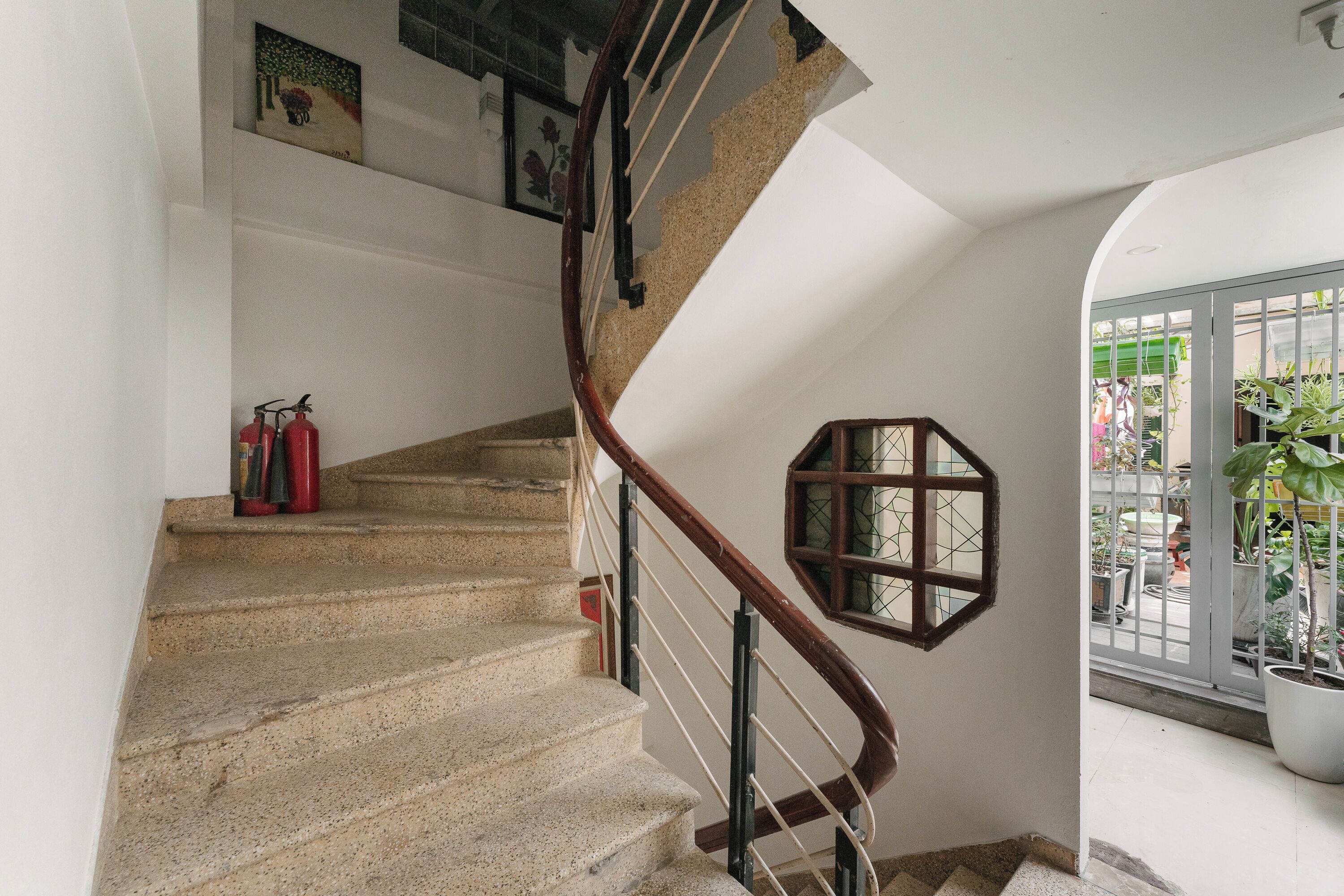 A staircase with a wooden handrail, a fire extinguisher on the landing, and a window with a geometric design.
