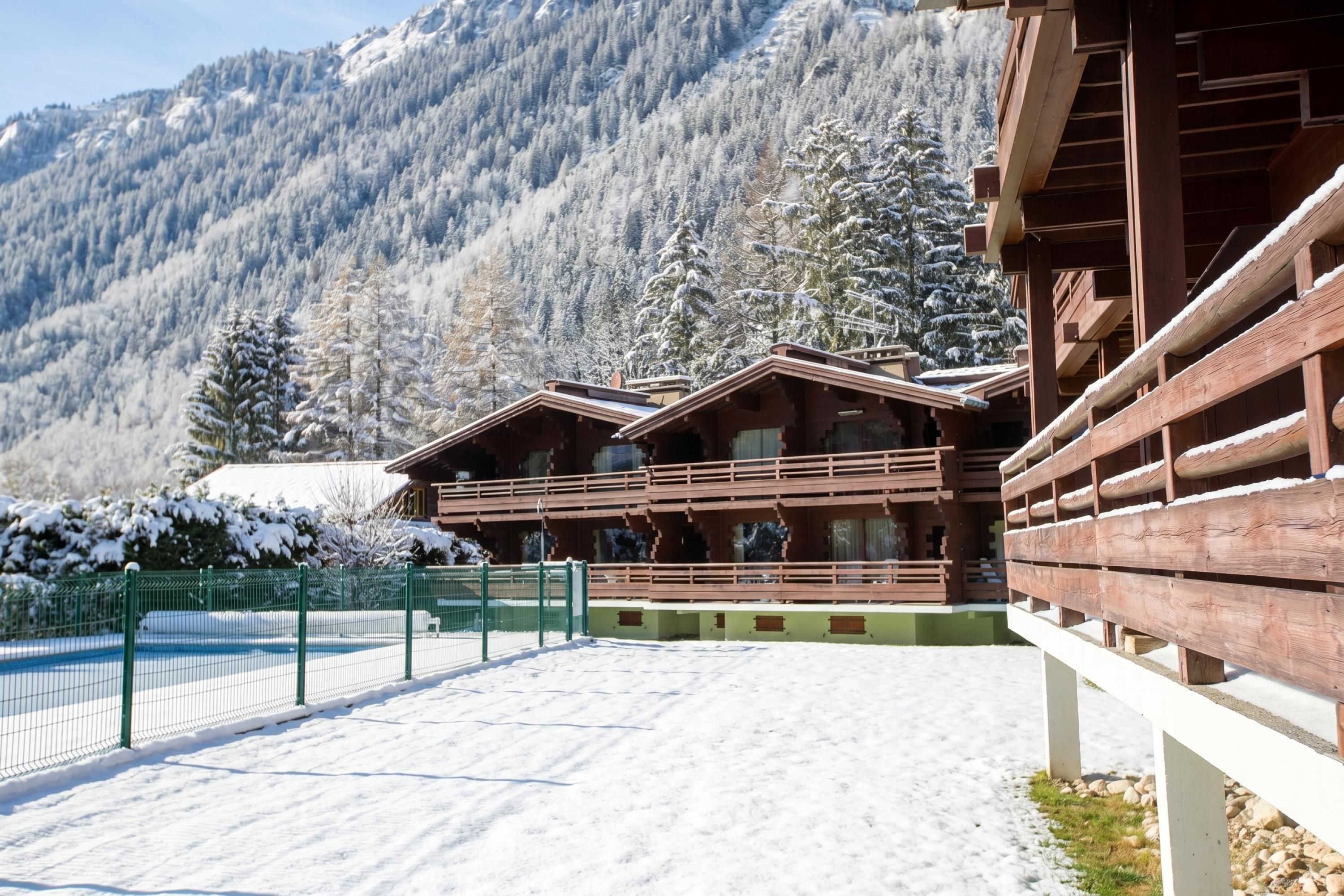 Eine Holzchalet mit Balkon, umgeben von schneebedeckten Bäumen und einer Bergkulisse.
