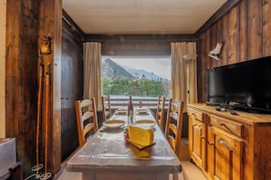 A dining area with a table set for six, a television, and a view of mountains through a window.