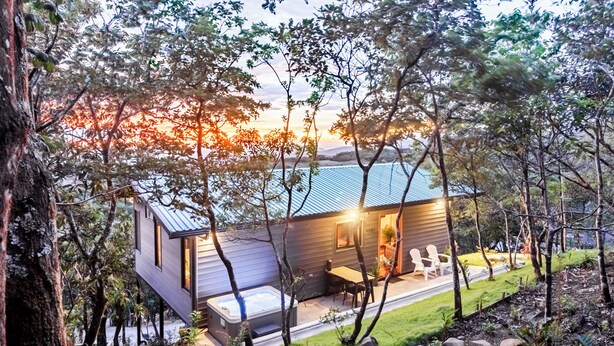 Een modern huis met een jacuzzi, houten terras en uitzicht op de zonsondergang.