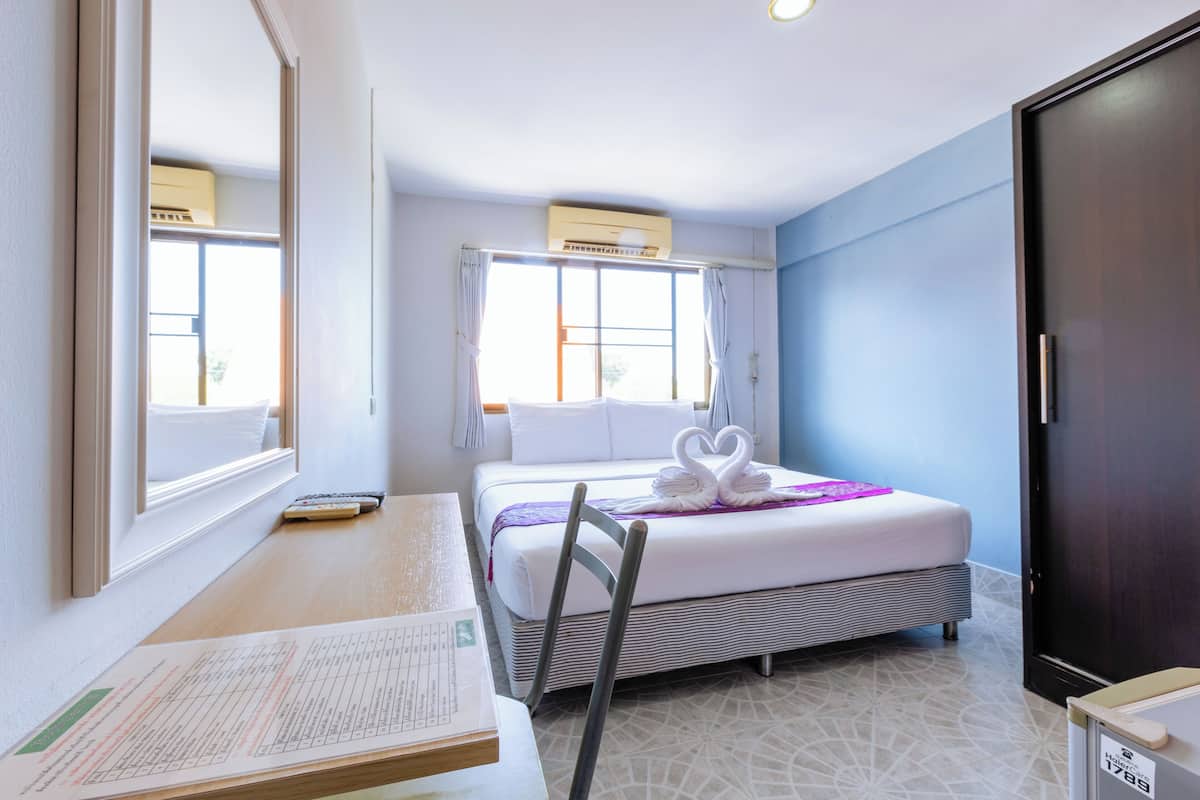 A hotel room with a bed, a desk with paperwork, a chair, a window with curtains, and a wardrobe.
