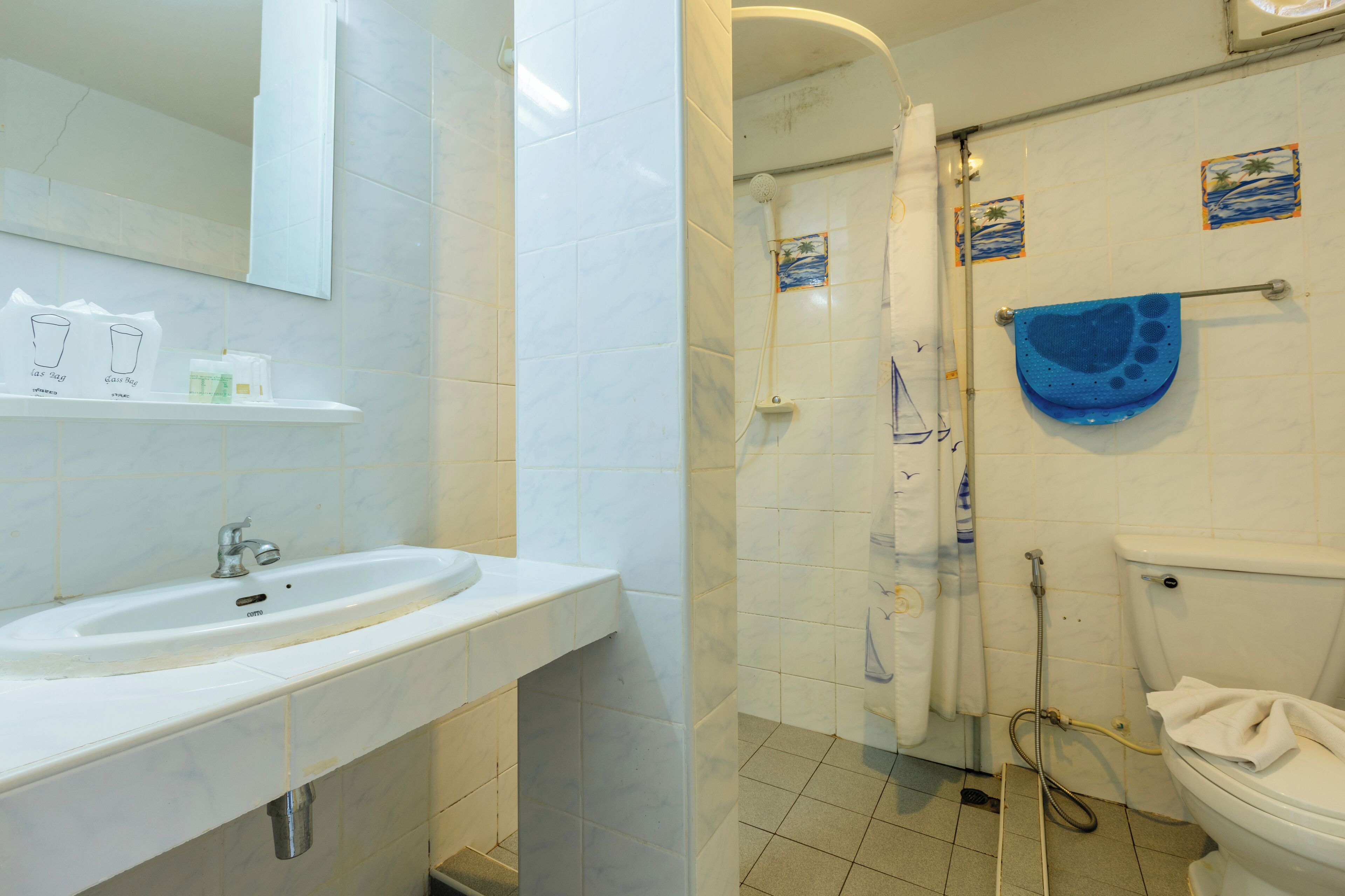 Et badeværelse med en hvid vask, spejl og toilet. Der er to små dekorative fliser på væggen.