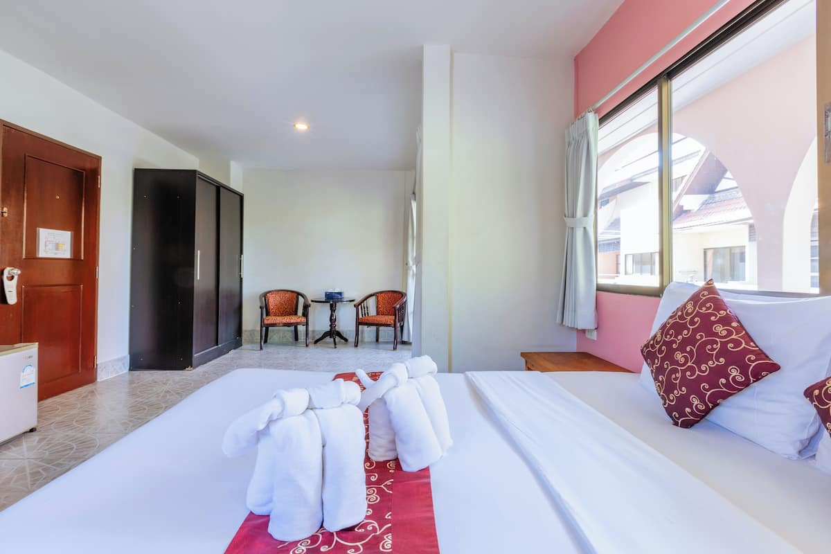 A hotel room with a neatly made bed, a small table with two chairs, and a view of the outside through a large window.