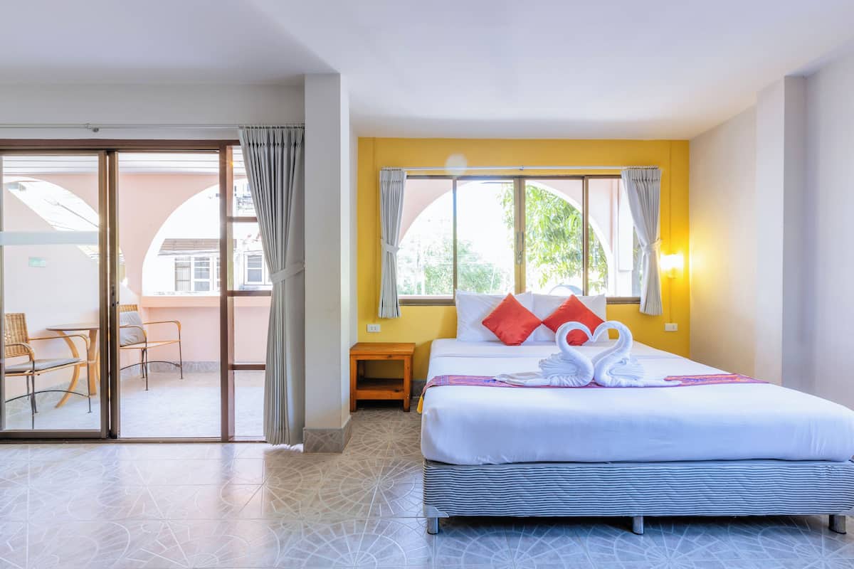 A hotel room with a bed, a small table, a chair, and a sliding glass door leading to an outdoor area.