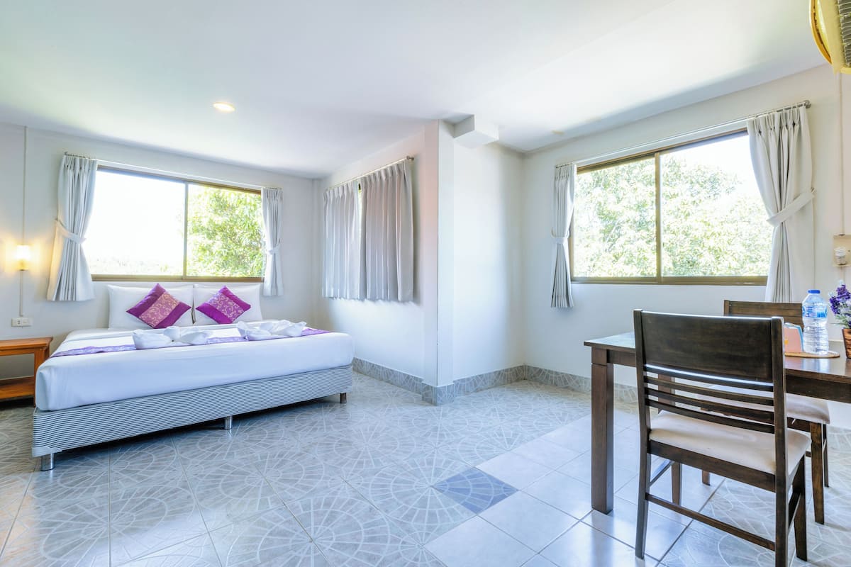 A hotel room with a bed, a dining table, and two windows with curtains.