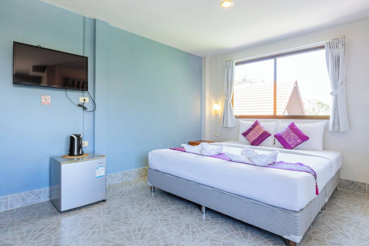 A hotel room with a bed, a TV mounted on the wall, a coffee maker, and a window with curtains.