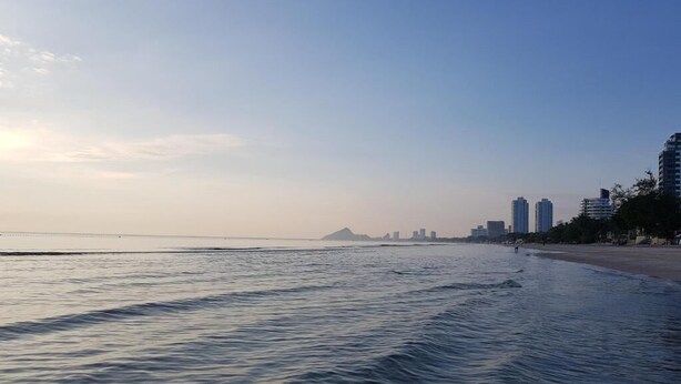 A beach with a calm sea, a distant mountain, and high-rise buildings along the shore. - Huahin Star Hotel (Hua Hin)